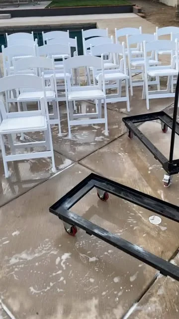 Rows of white folding chairs on a wet patio beside a pool