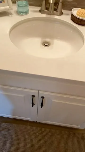 A white bathroom vanity with a clean oval sink and black handles